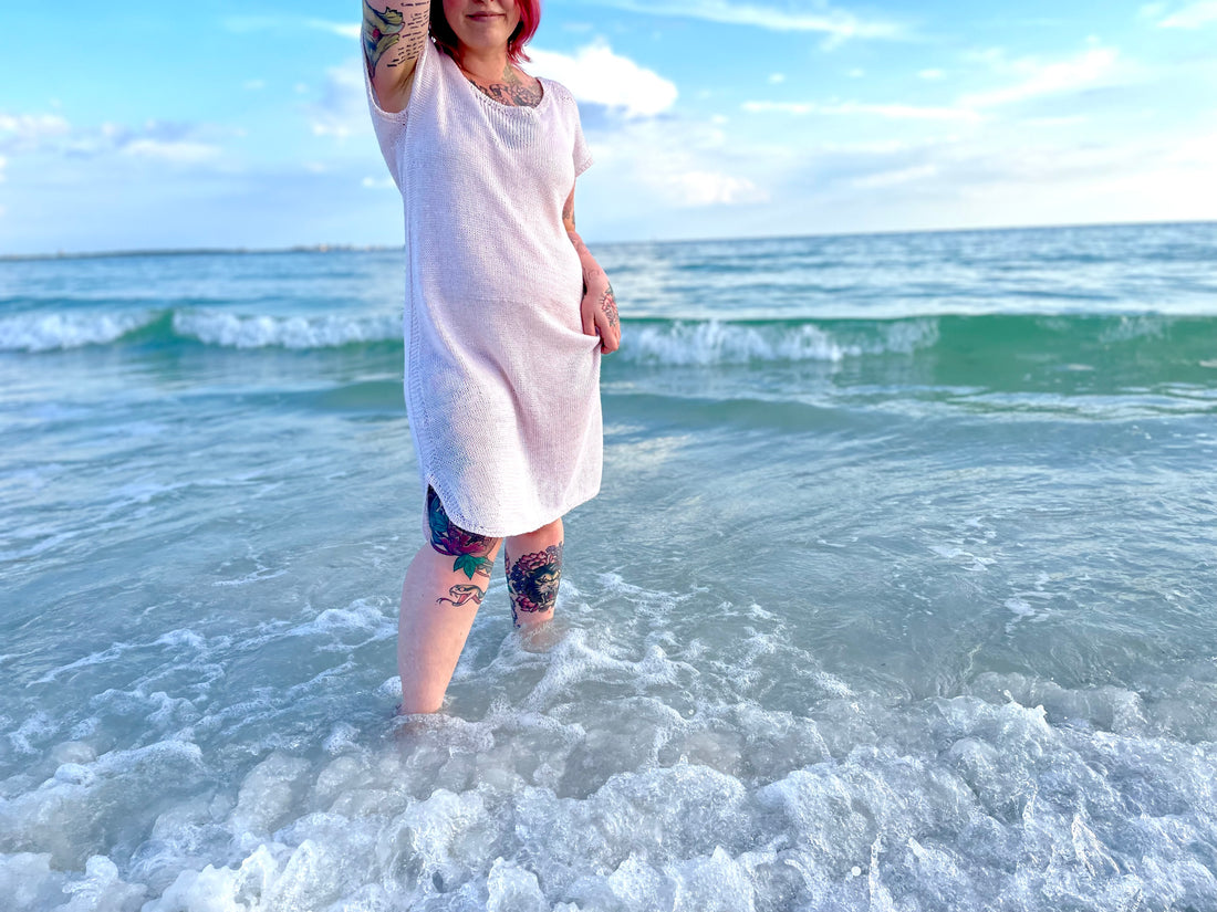 Elizabeth wears a tencel dress knit from a dress knitting pattern she is standing on the beach in the ocean