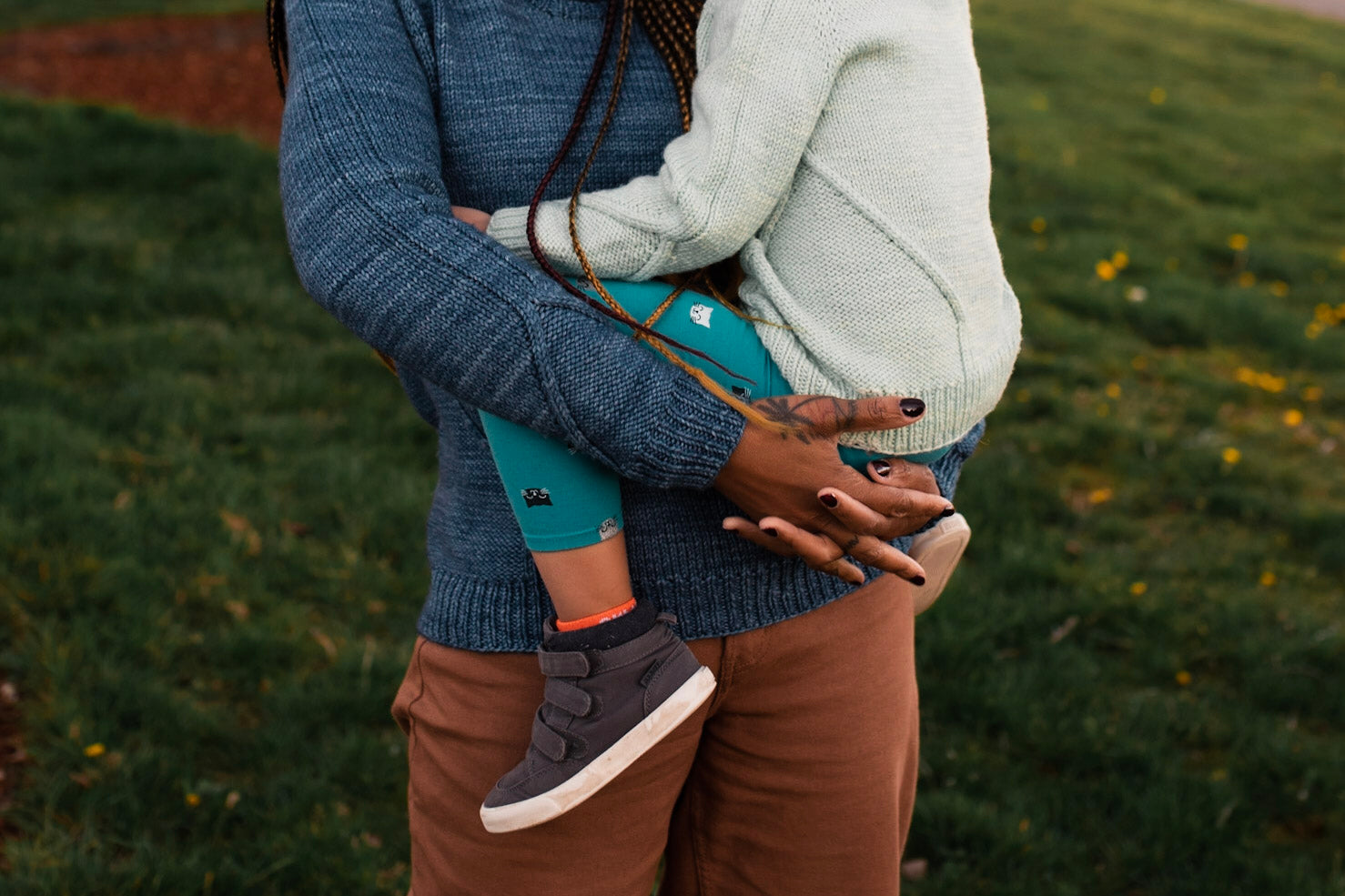 Rachel holds Mia in her arms, the camera focusing on the cable design around the cuffs of her navy blue, hand knit sweater.