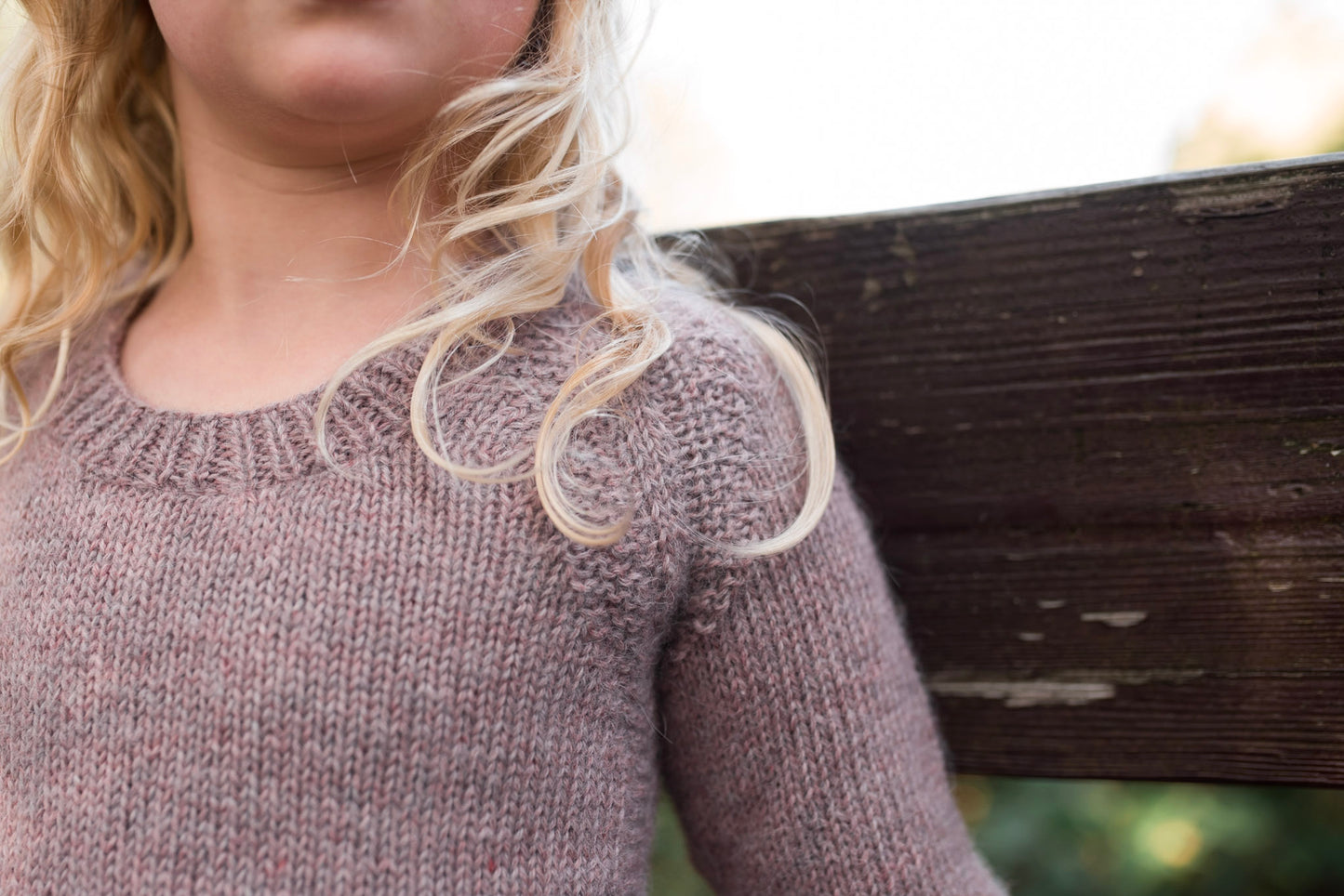 Seen close up, a girl wears a light purple knit sweater. A garter stitch embellishment is knit around the seams.