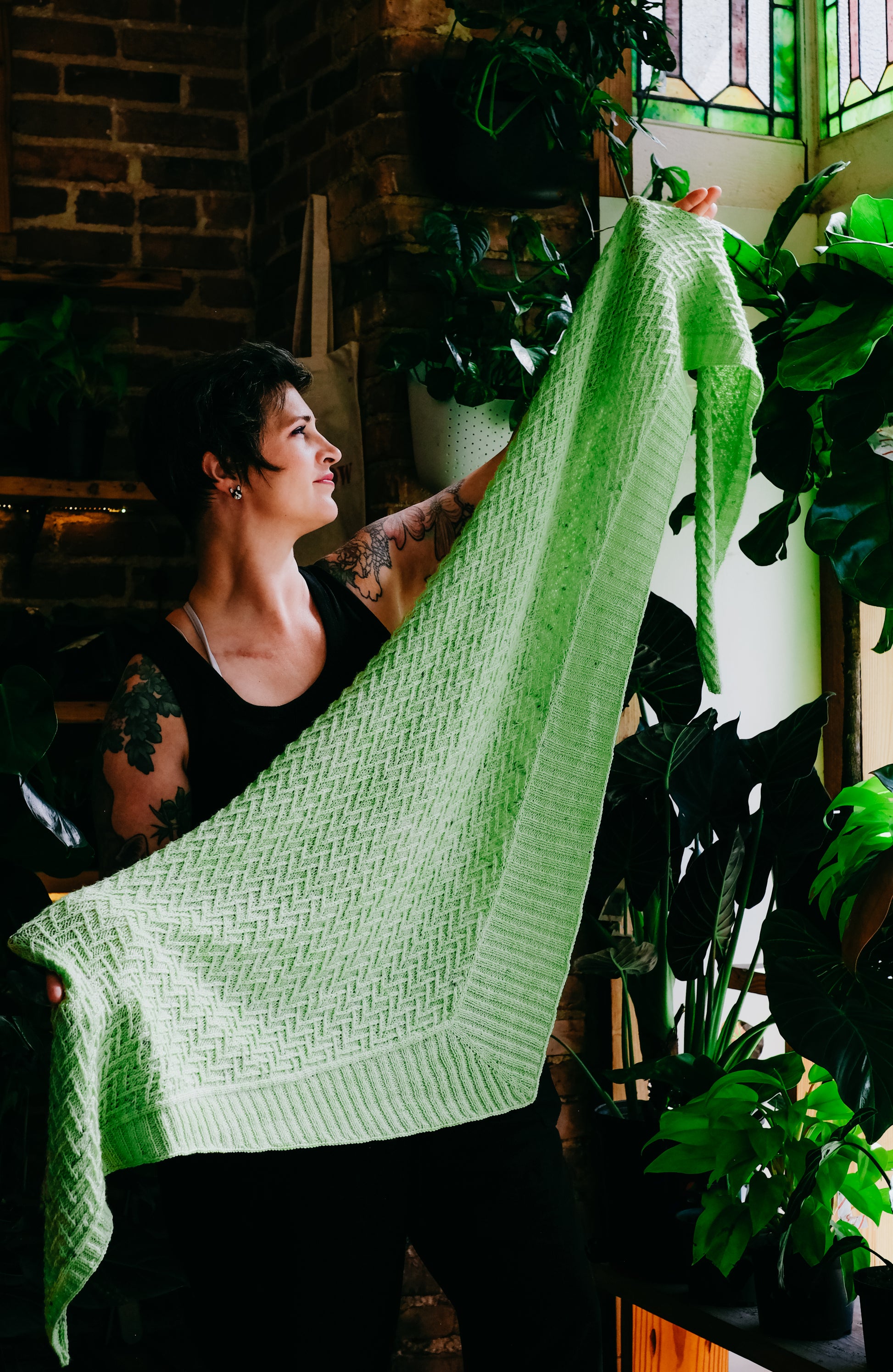 Jen holds open a asymmetric triangle shawl, knit with lime green yarn. The shawl has an all-over chevron stitch design with a ribbed edging on two sides of the triangle.