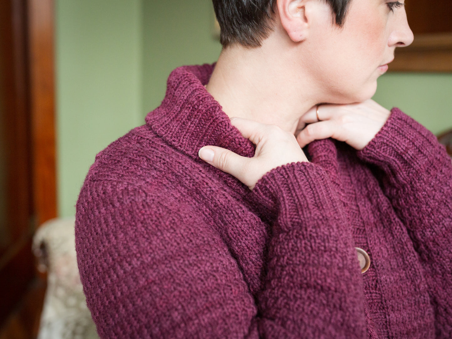 Seen up close, Jen holds the ribbed cowl neck of her cardigan, knit with burgundy yarn in a subtle all-over stitch. 
