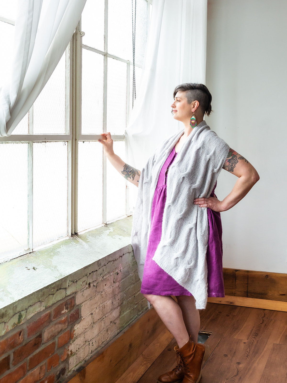 Seen from the side, Jen stands in front of a window, wearing a magenta dress under a light blue rectangle shawl, knit with fluffy yarn.