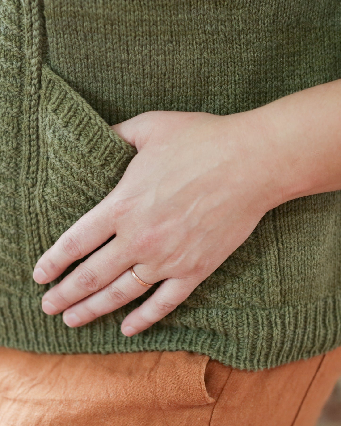 Seen close up, Jen has her thumb tucked in the pocket of her hand knit, green cardigan. The diagonal of the pocket is approximately the length of her hand.