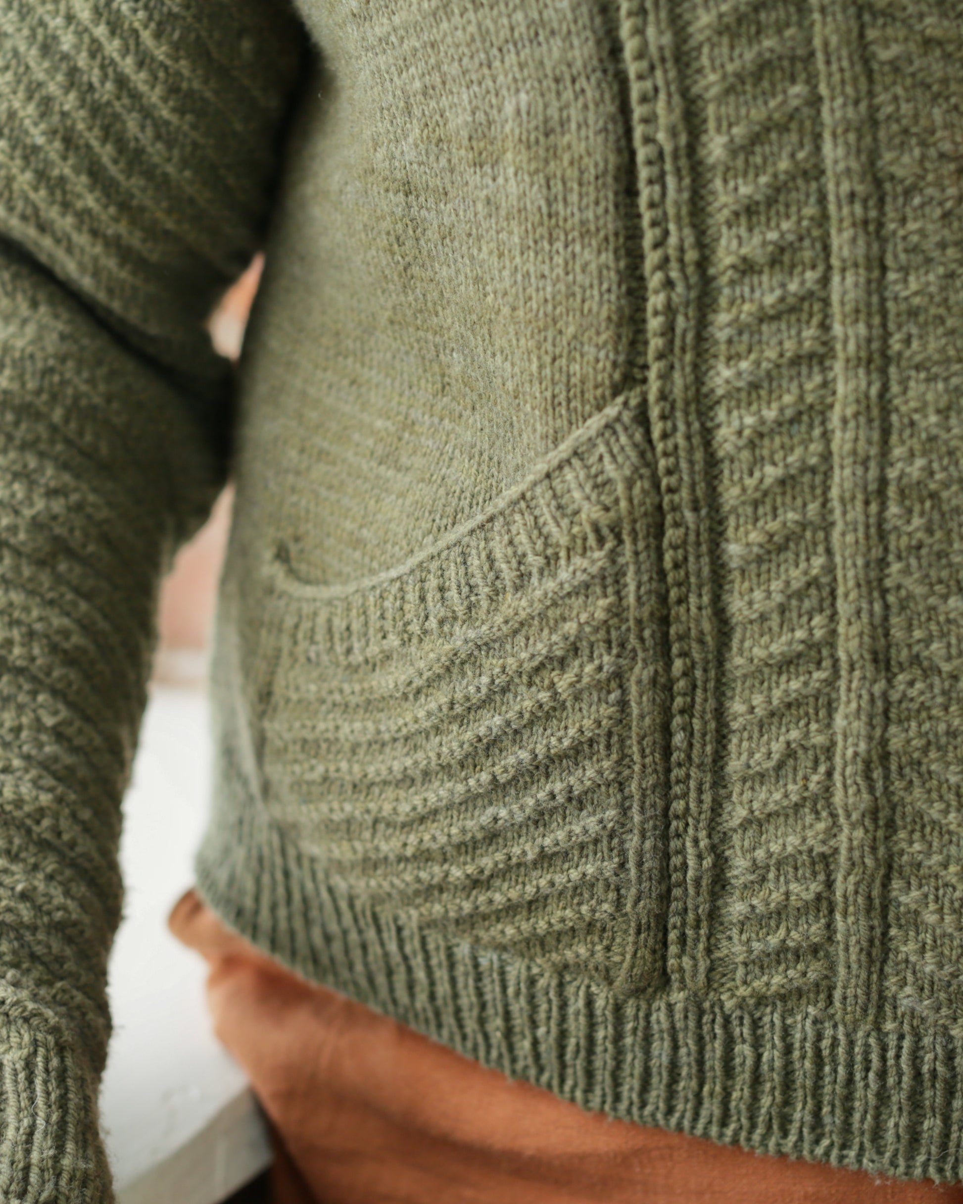 Seen up close, Jen wears a green cardigan with a chevron design. The camera focuses on the slanted front pocket.