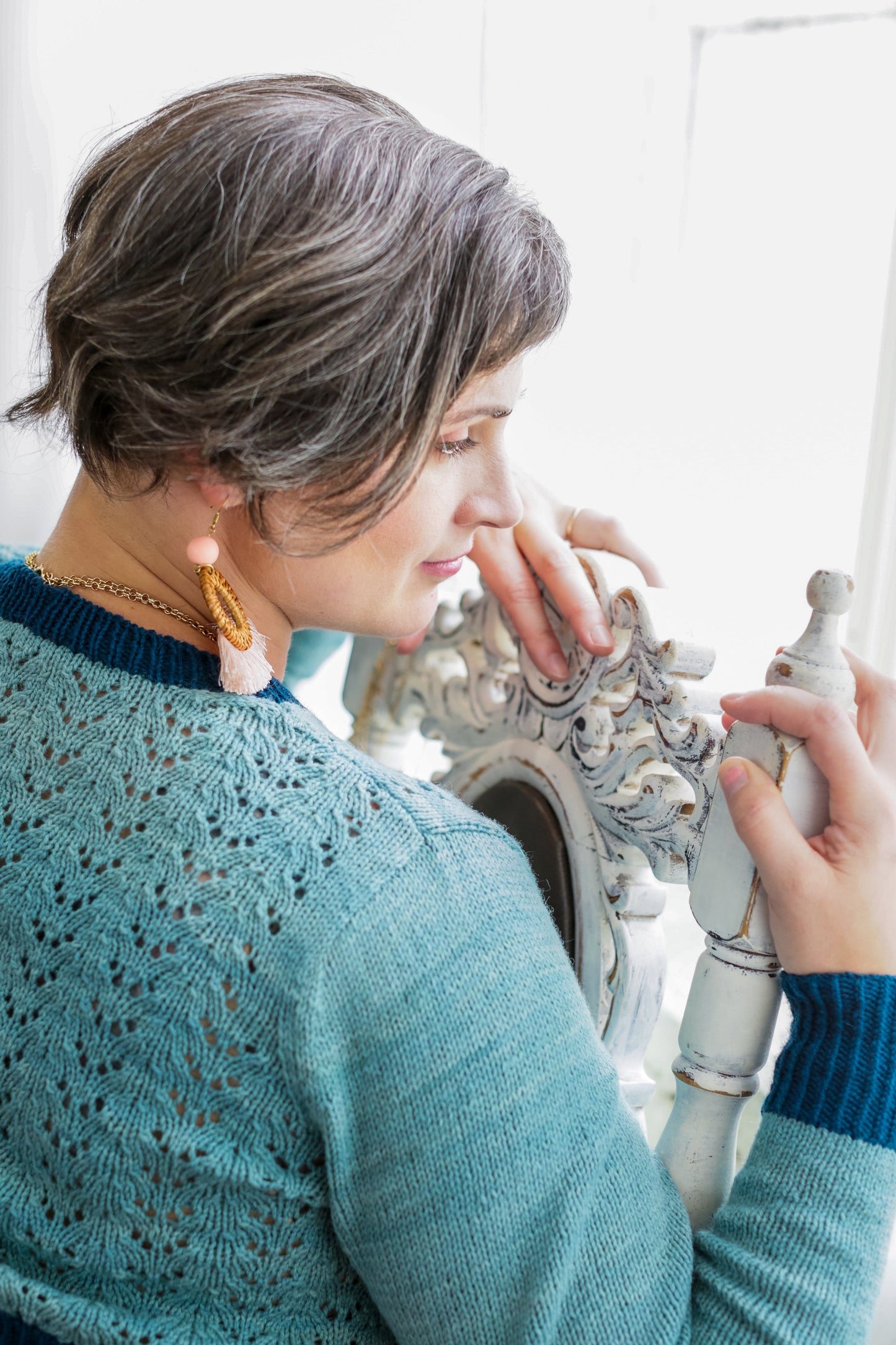 Seen close up from behind, Jen wears a light blue sweater, knit with dark blue cuffs and neckline. The sweater features a lace design on the body.