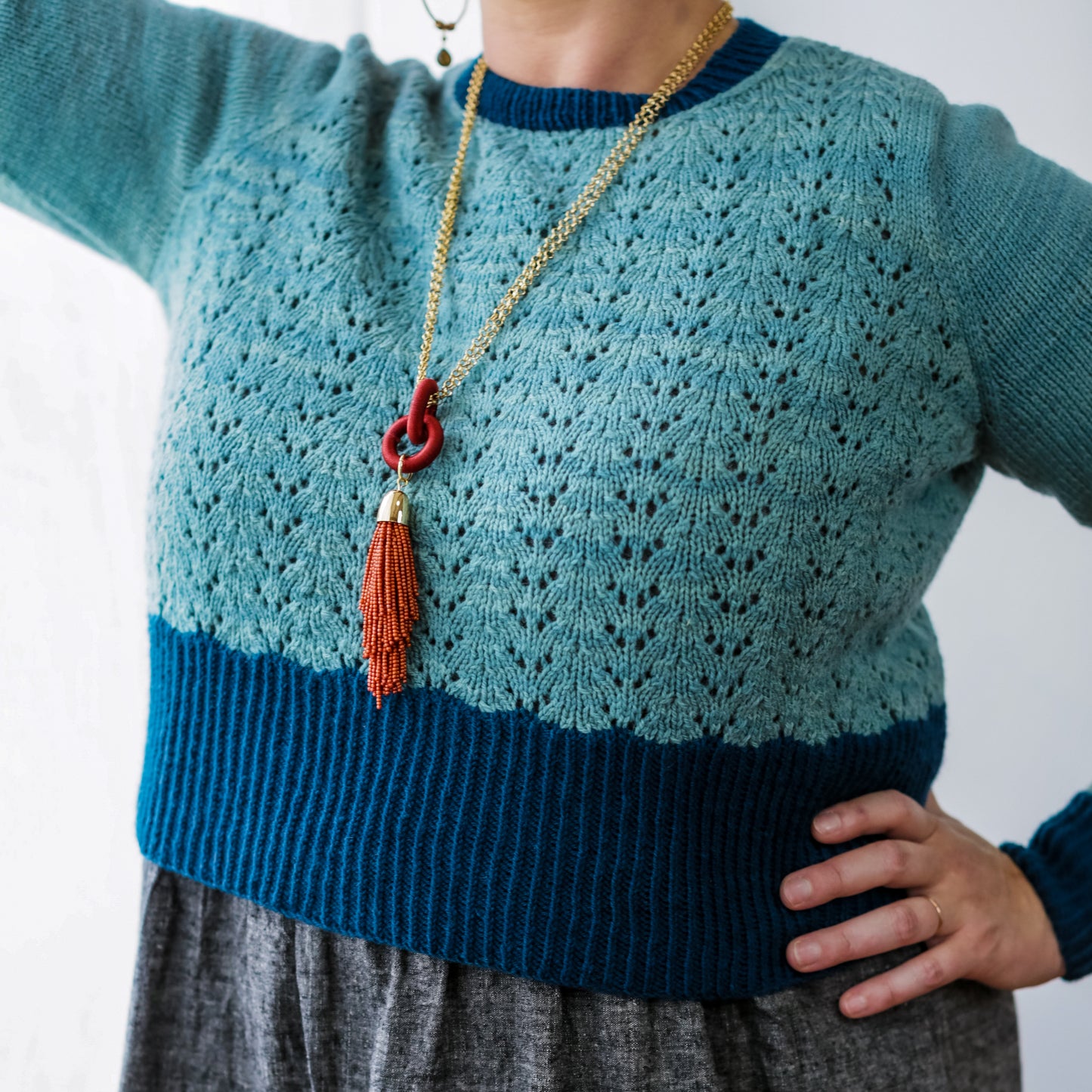 Seen from the shoulders down, Jen wears a cropped pullover, knit with light blue yarn in a lace deisgn and a dark blue hem, cuffs, and neckline. 