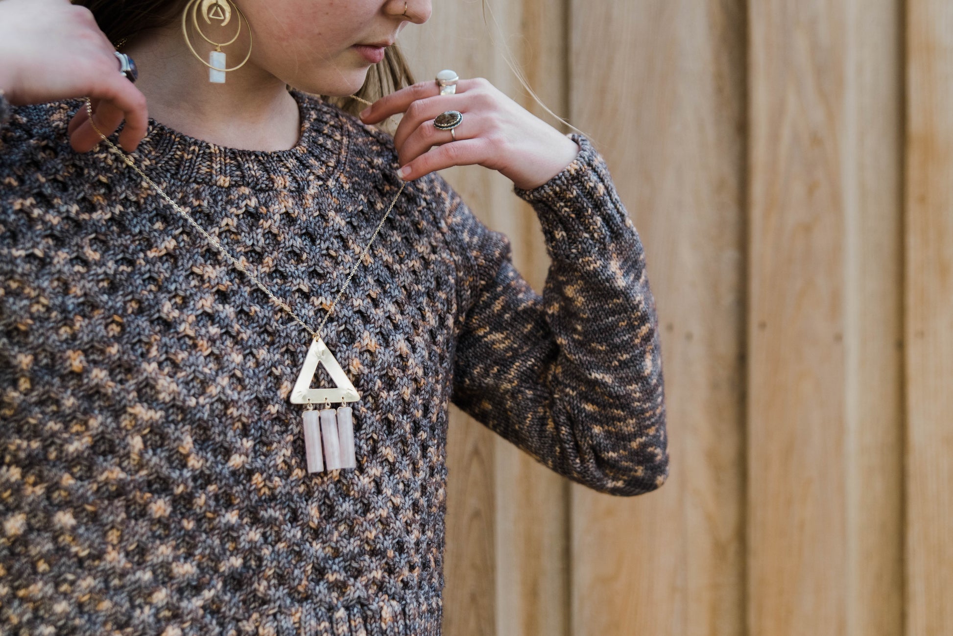 Haley puts on a large triangle pendant necklace. She wears a sweater, knit with variegated brown yarn that's designed with a honeycomb stitch pattern on the body.
