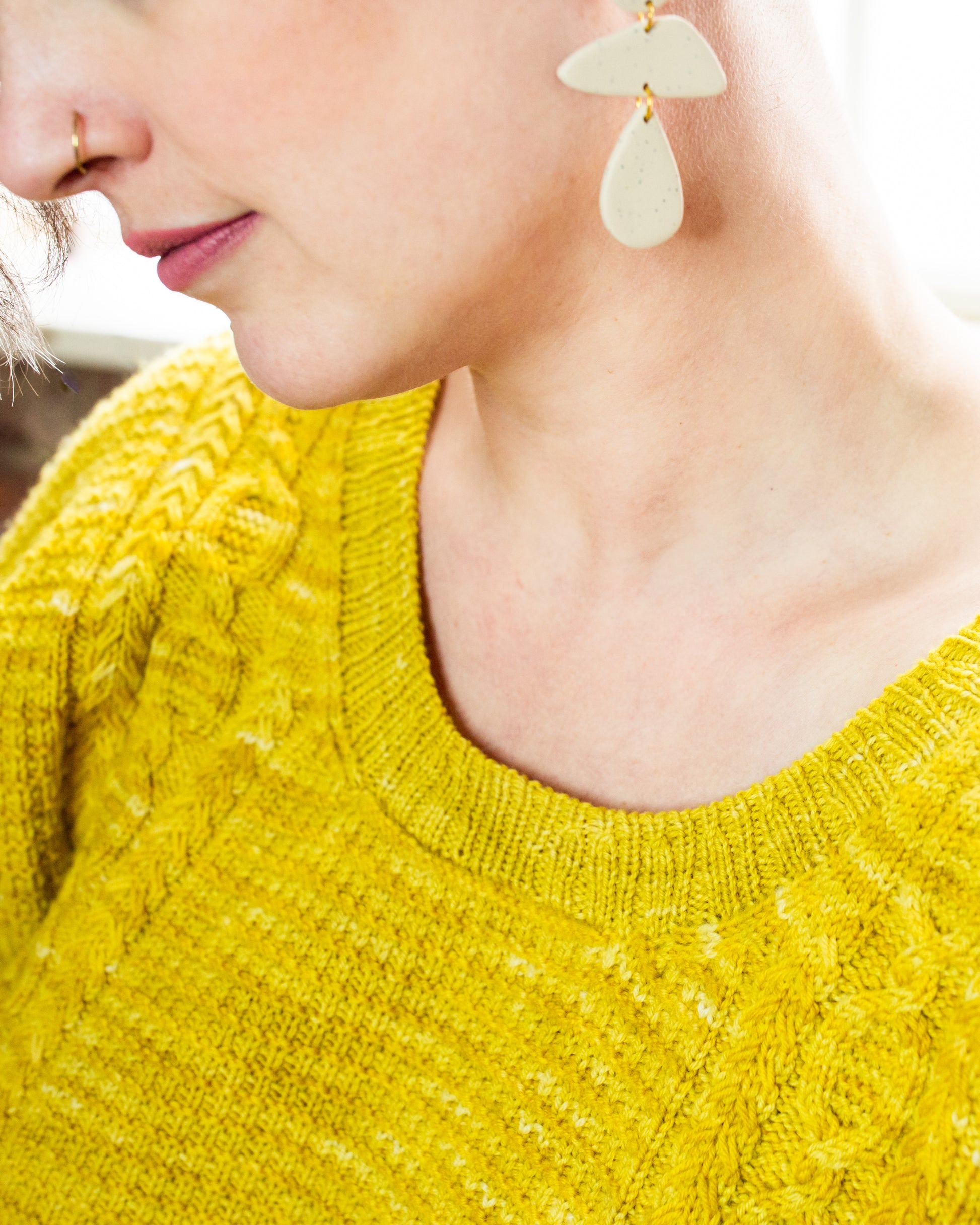 Seen close up, Jen wears a bright yellow sweater, knit with a scoop neck and cable strips that surround a seed stitch panel.