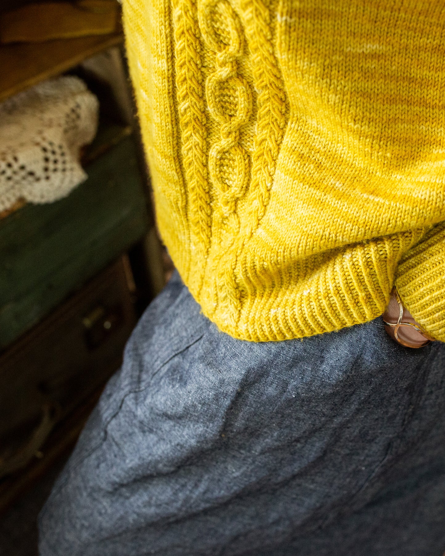 Jen wears a bright yellow sweater with wide leg blue pants. The camera focuses close up on the ribbed hem and cable strip design.