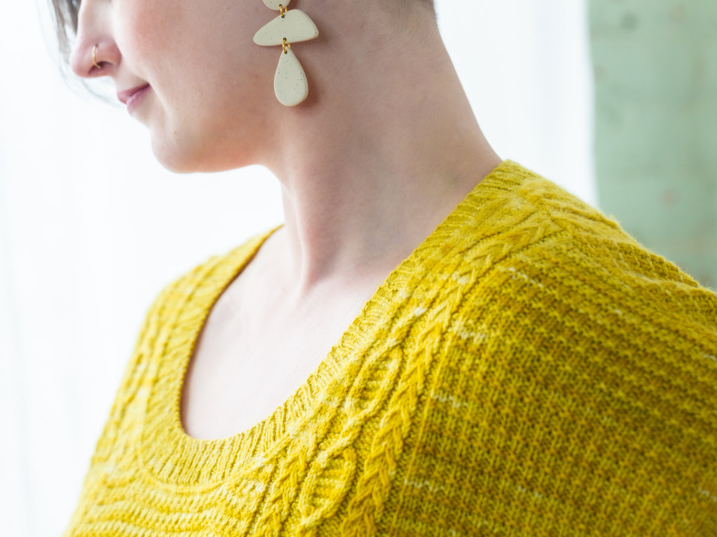 Seen close up, Jen wears a pullover, knit from bright yellow yarn, that has a cable and seed stitch texture.
