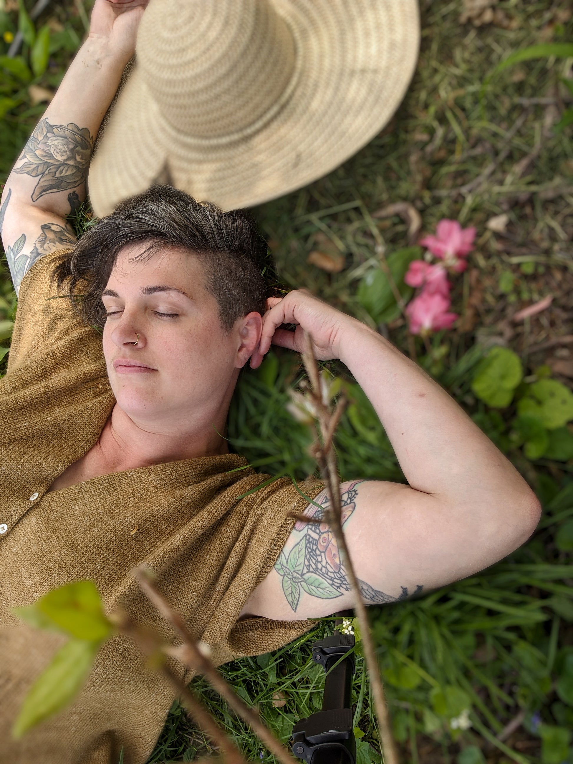Jen lays in the grass, eyes close. She wears a gold dolman tee, buttoned with pearl buttons - the Gone to Seed tee.