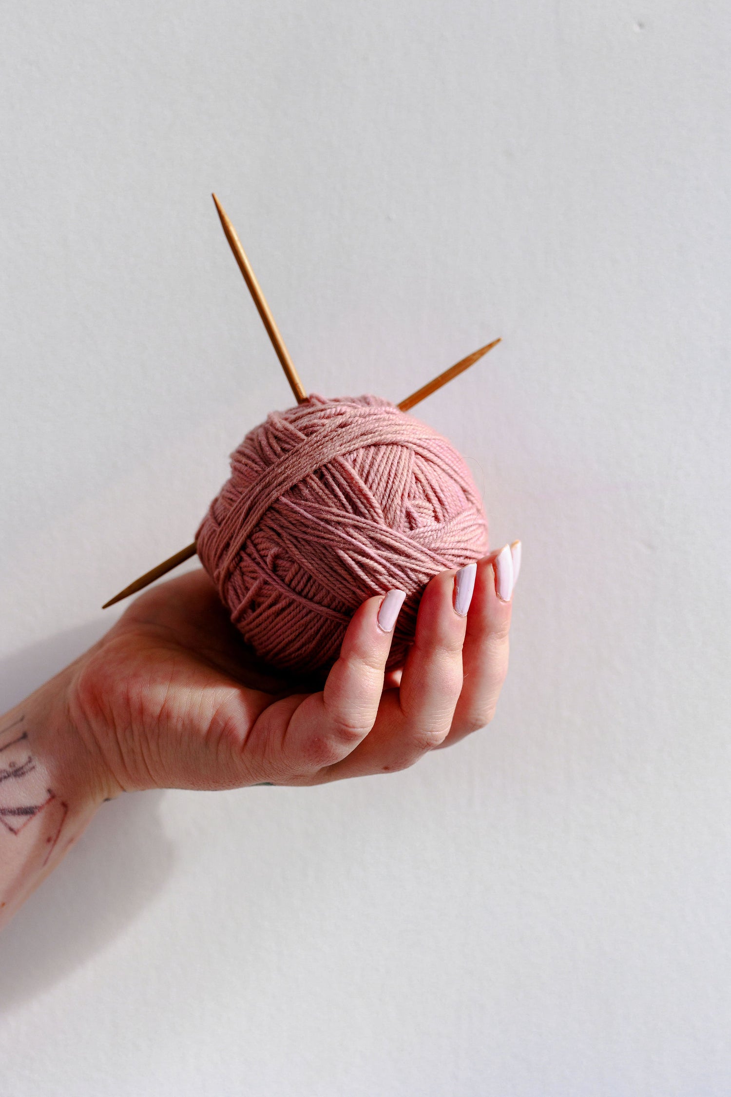 Bess' hand holds a pink ball of yarn, with two knitting needles in it.