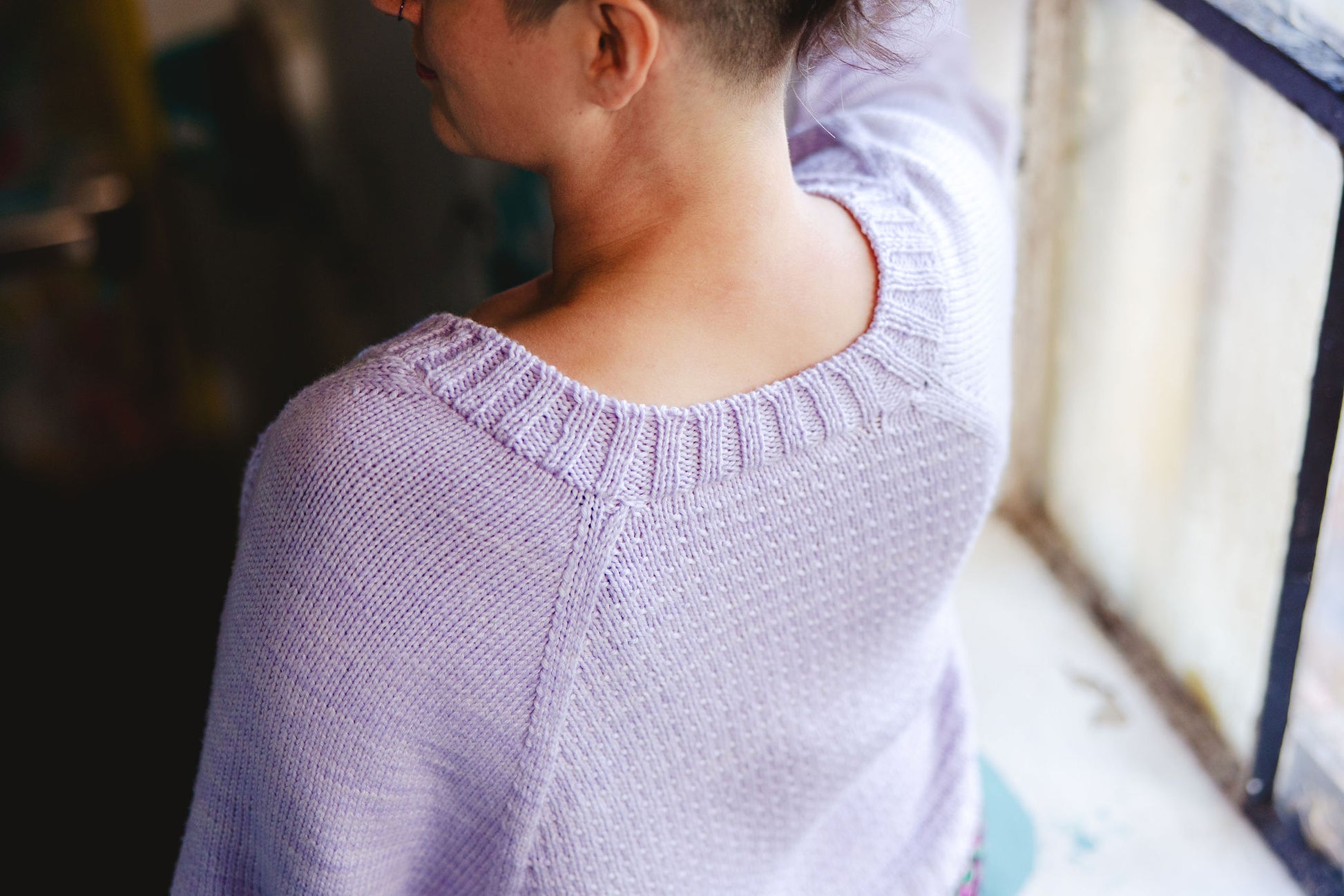 Seen from behind, Jen poses to show off the scooped back neckline of her light purple knit sweater.