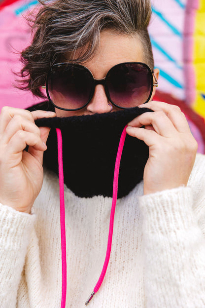 Wearing sunglasses, Jen holds up the black collar of her white hoodie, showing off the pink sweater strings and fluffy yarn.