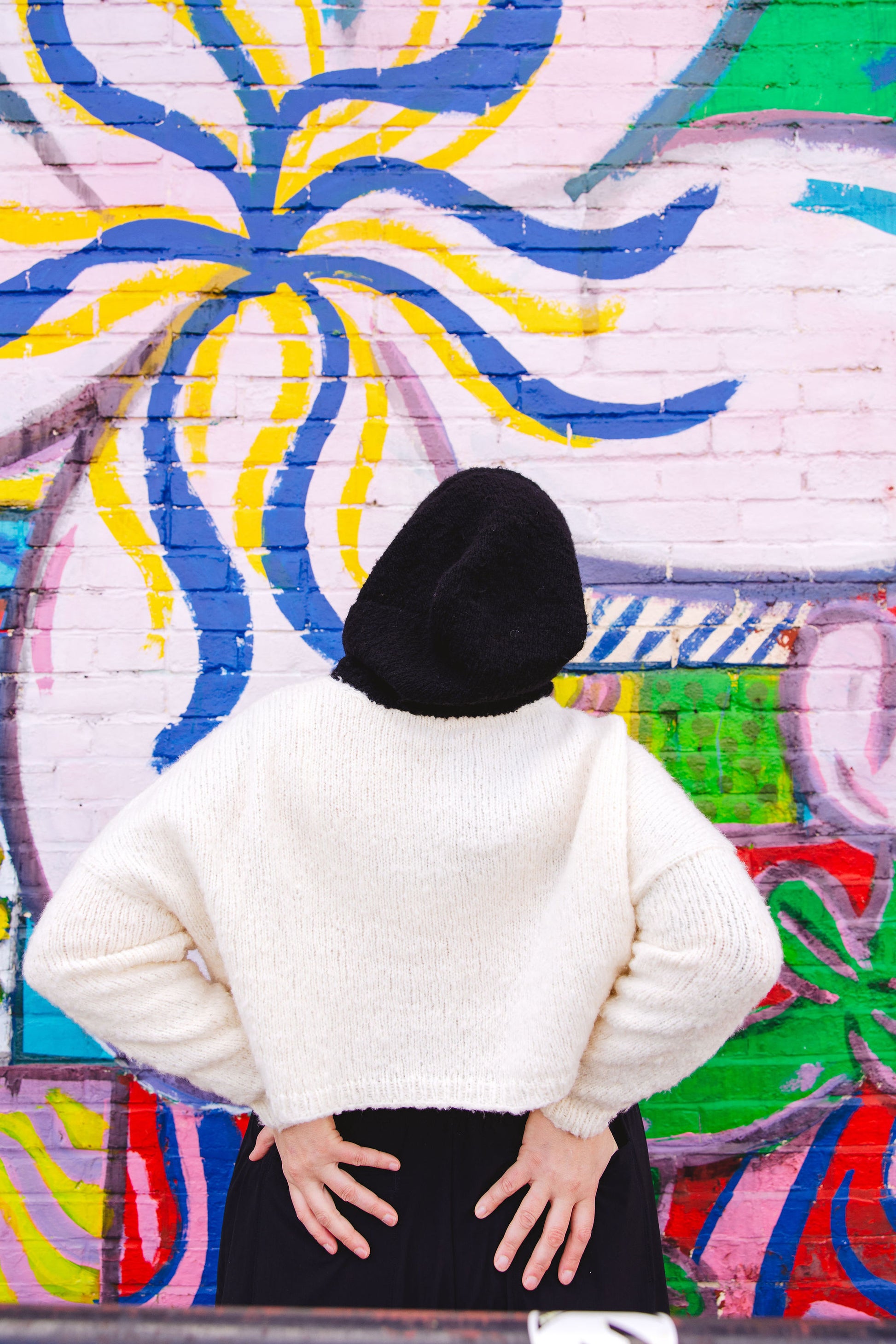 Seen from behind, Jen wears a black and white hoodie, knit from super soft yarn. A wall mural can be seen in the background.