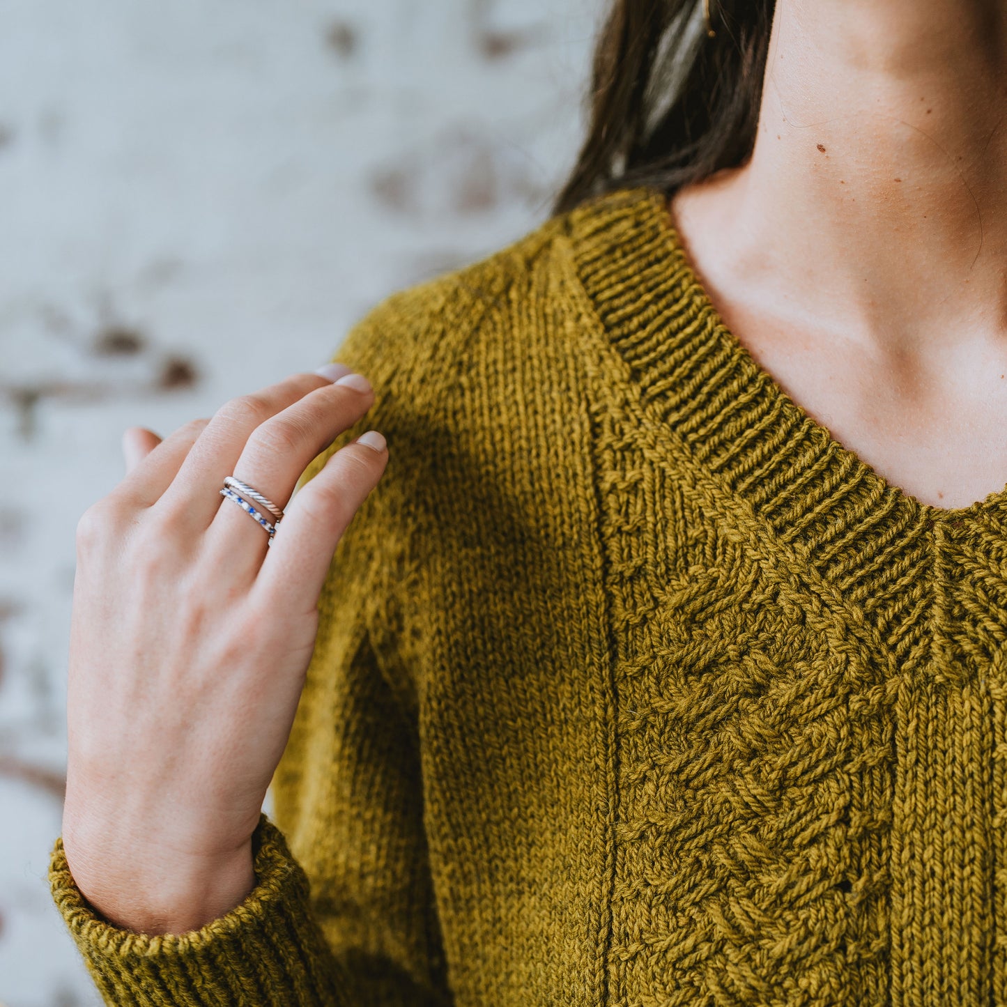 Seen from up close, the camera focuses on the cabled details of the knit sweater Laura is wearing. The yarn is a golden color.