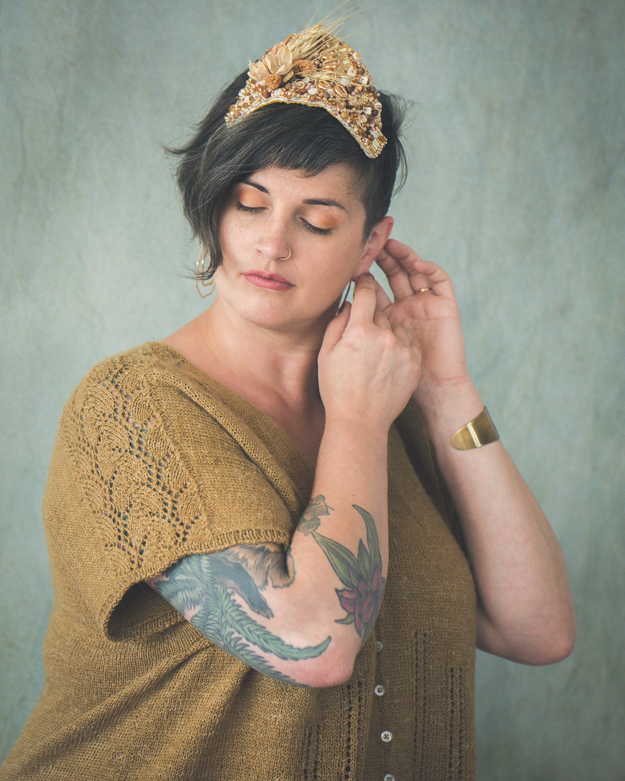 Jen turns to the side, adjusting her gold earrings. The angle shows off the leafy lace panel on the sleeve of her gold, knit dolman tee. The shirt is closed with five pearl buttons down the front, which are outlined by eyelet lace strips.