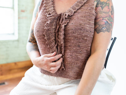 Jen wears a dusty pink tank top, seen close up. the top has a delicate ruffle collar and a ribbed hem. 