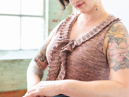 Jen sits, wearing a pink, ruffled, tank top, knit from her Ruffle Addendum pattern.