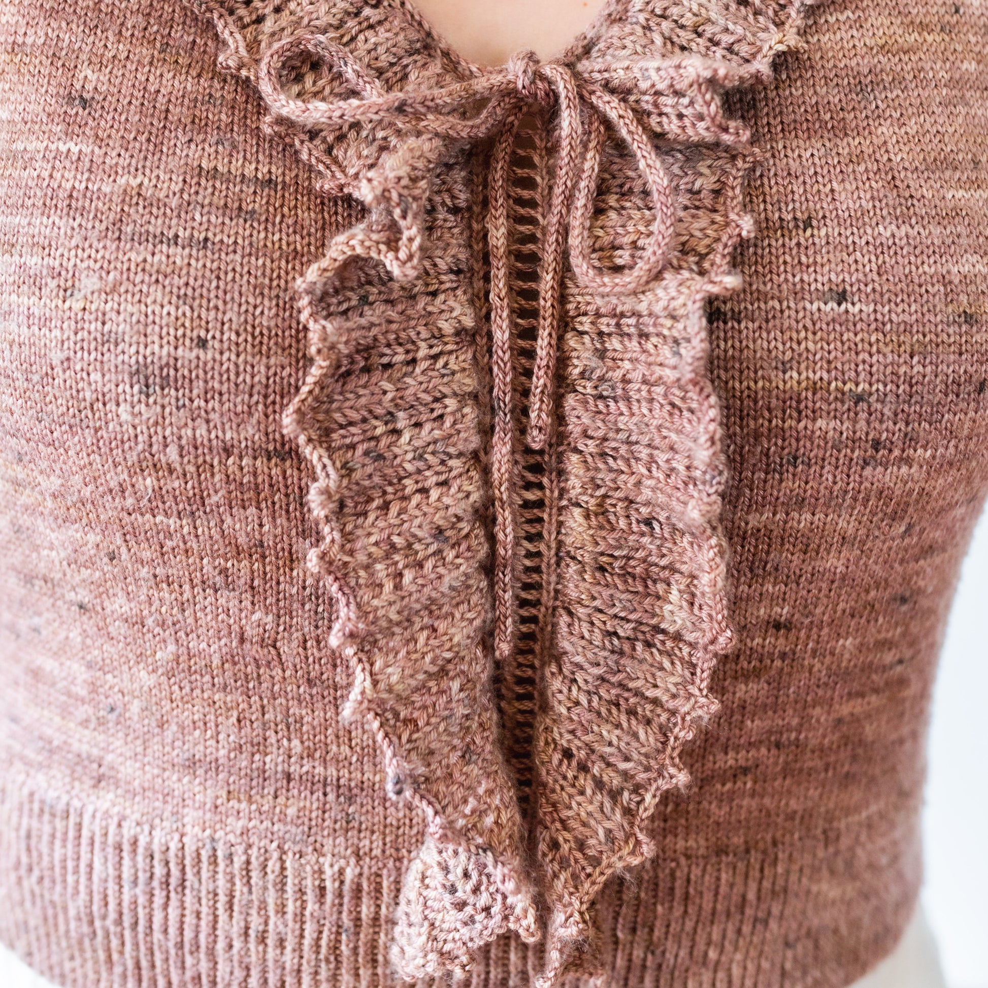 Seen up close, Jen wears a pink knit tank top. The lace details on the ruffle and bow tie can be seen in detail.