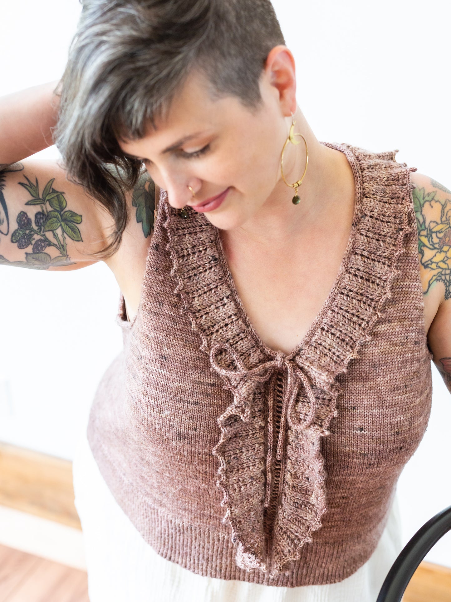 Seen from above at an angle, Jen wears a pink, hand knit tank. The top has a ruffled lace collar.