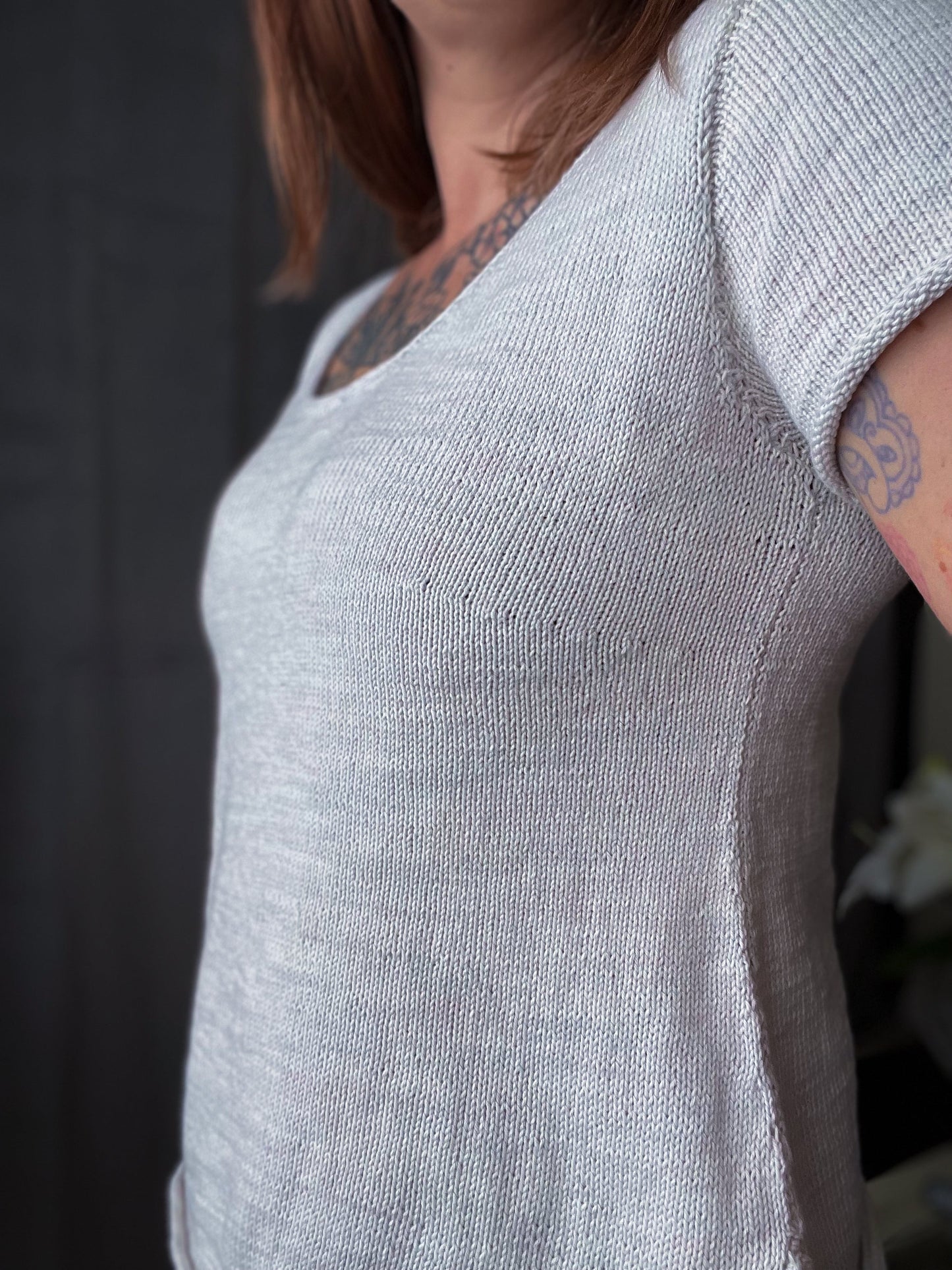 Seen from the side and from the shoulders down, Bess wears a white tee knit in a simple stockinette stitch.