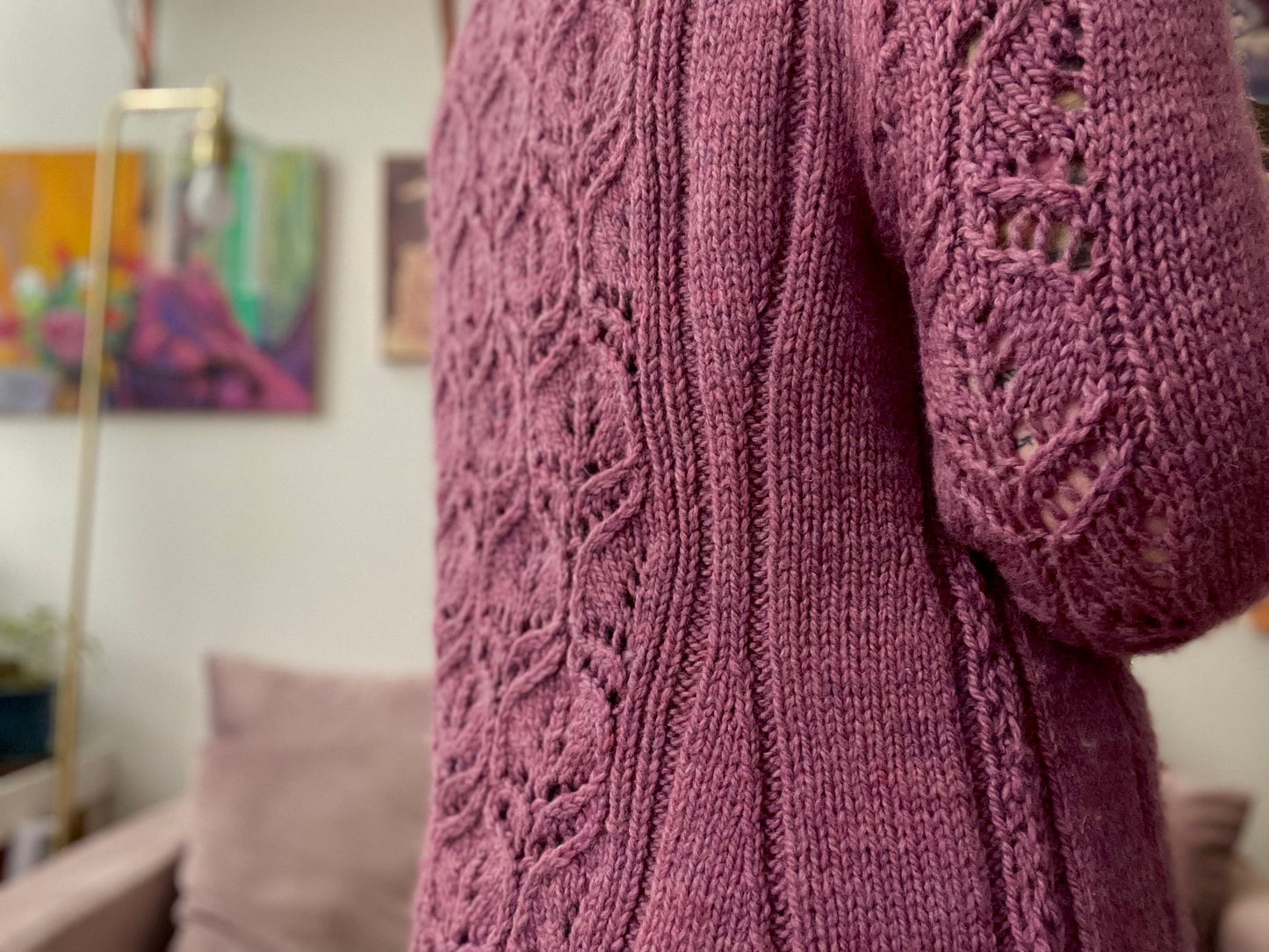 Seen close up, Bess wears a light pink cardigan. It's knit in bulky yarn with large lace panels down the arms and back.