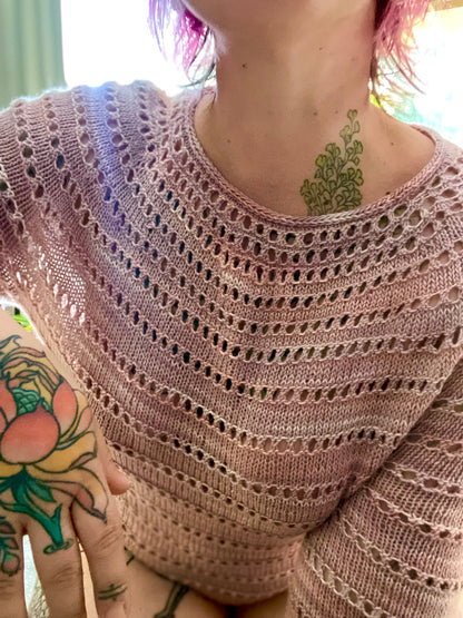 Bess leans towards the camera, showing off her hand knit sweater. The camera focuses on the details of the eyelet lace and the i-cord neckline.