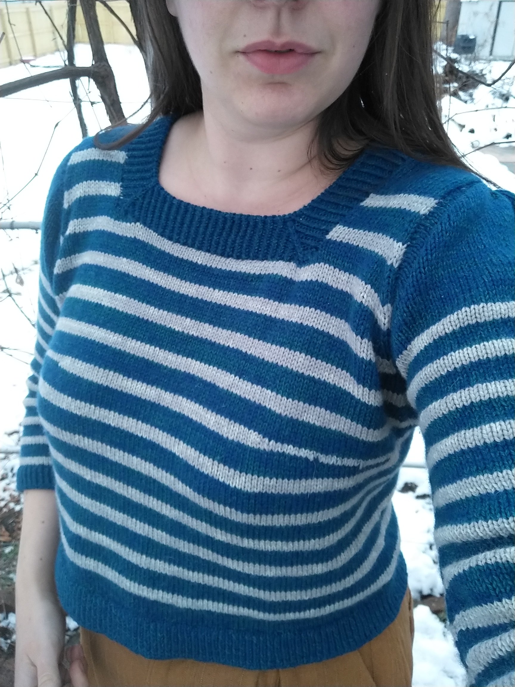 A person, seen from the neck down, wears a hand knit, blue and white striped sweater. The neckline is square and the sleeves are gathered at the top.
