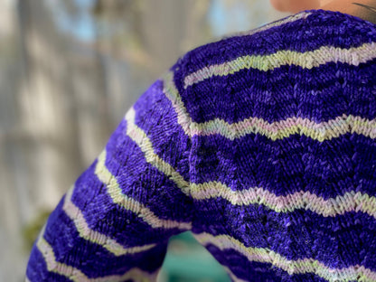 Seen close up, Bess wears a blue and white striped dress. The dress is knit with a feather and fan lace stitch.