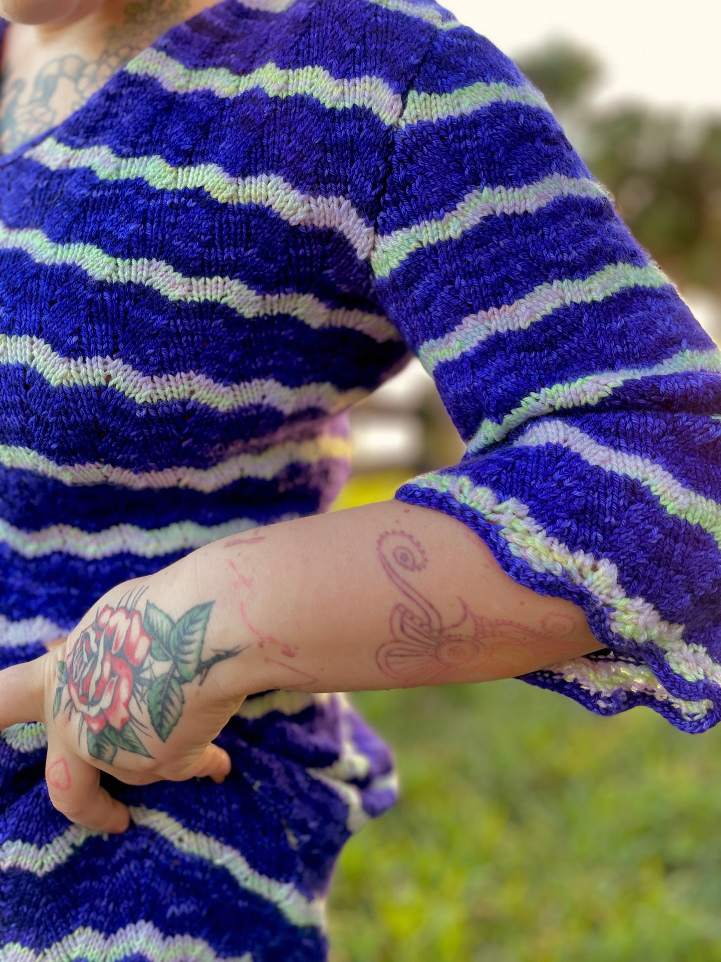 Seen close up, Bess wears a blue and white dress. The sleeves are knit at a 3/4 length, and the cuffs are slightly scalloped from the feather and fan lace stitch.