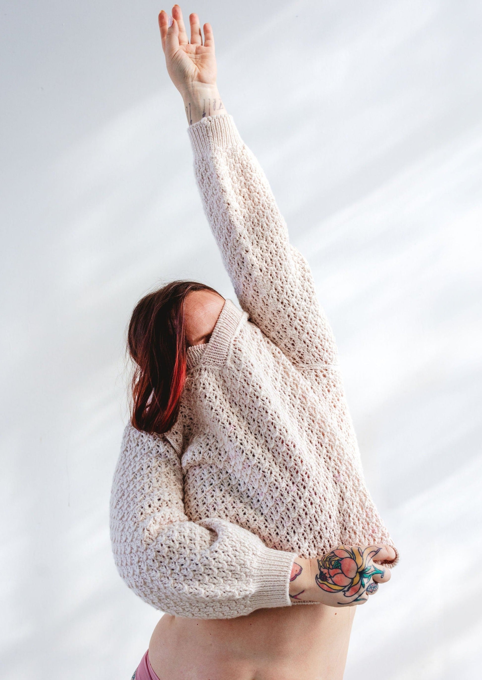 Bess pulls on a cream lace knit sweater, knit from the Mary Raglan pattern.