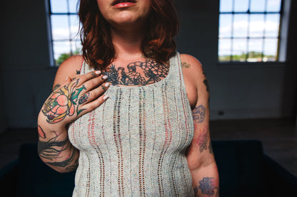 In dramatic lighting, Bess stands in front of the camera. She wears a chevron lace knit tank top, knit from the Tori Tank pattern.