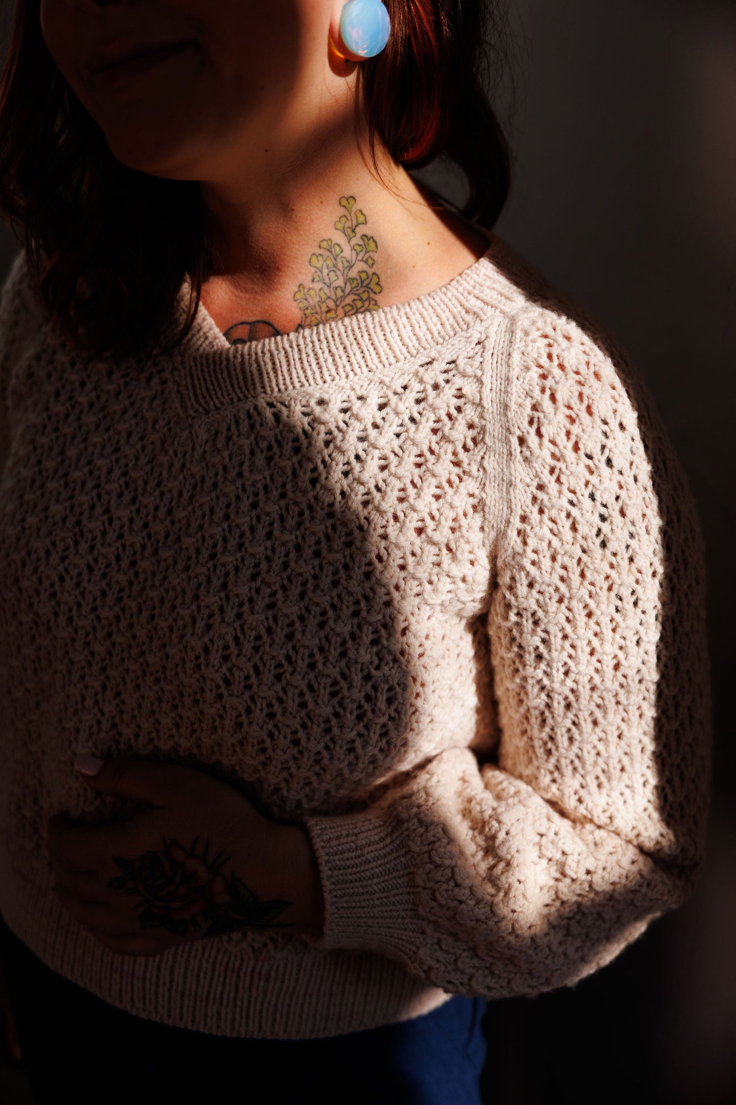 Dramatic lights highlight Elizabeth's neck and shoulder. She is wearing a lace knit sweater that she knit from the Mary Raglan pattern.