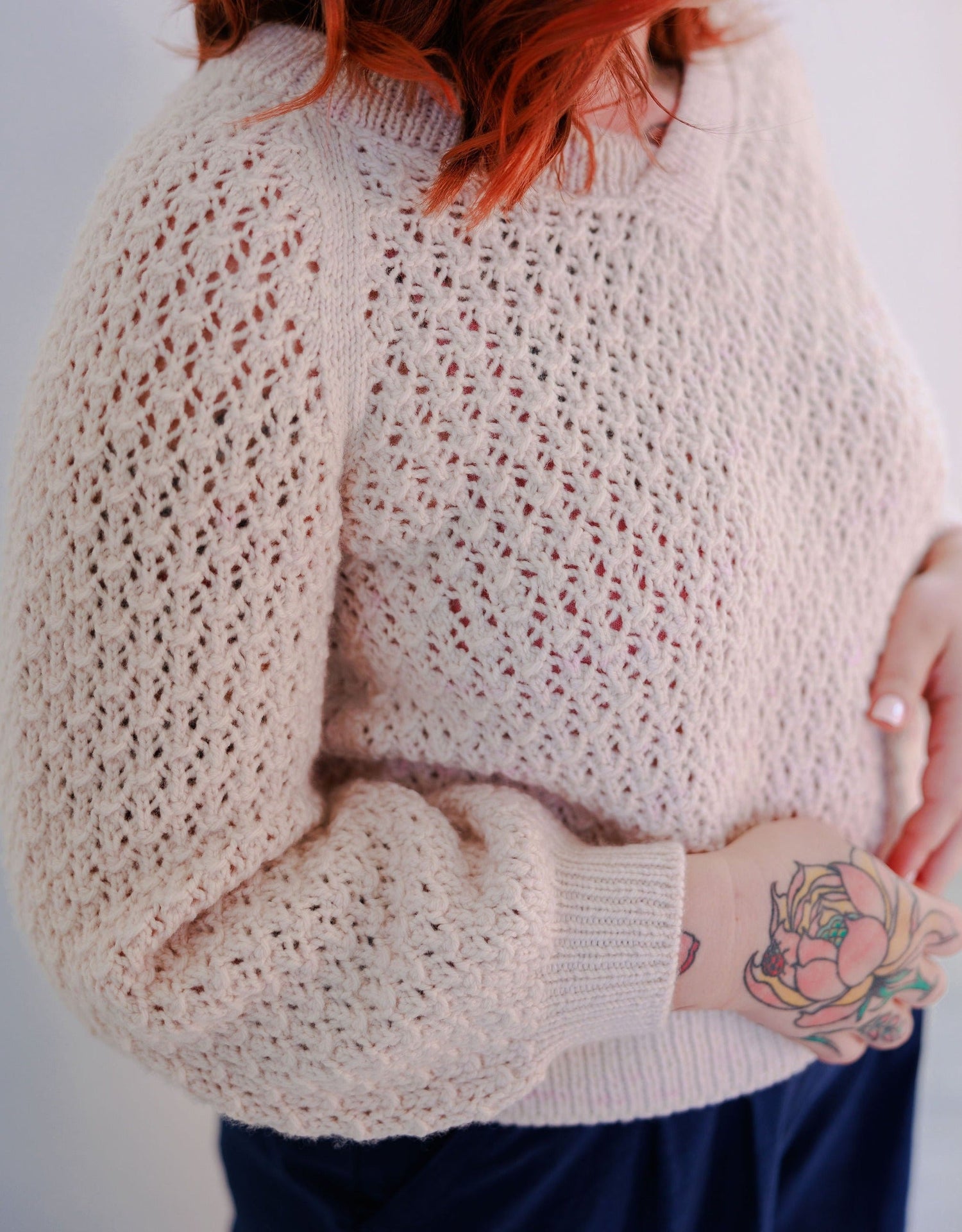 Bess stands at a 3/4 angle to the camera, wearing a cream colored lace knit sweater, the Mary Raglan.