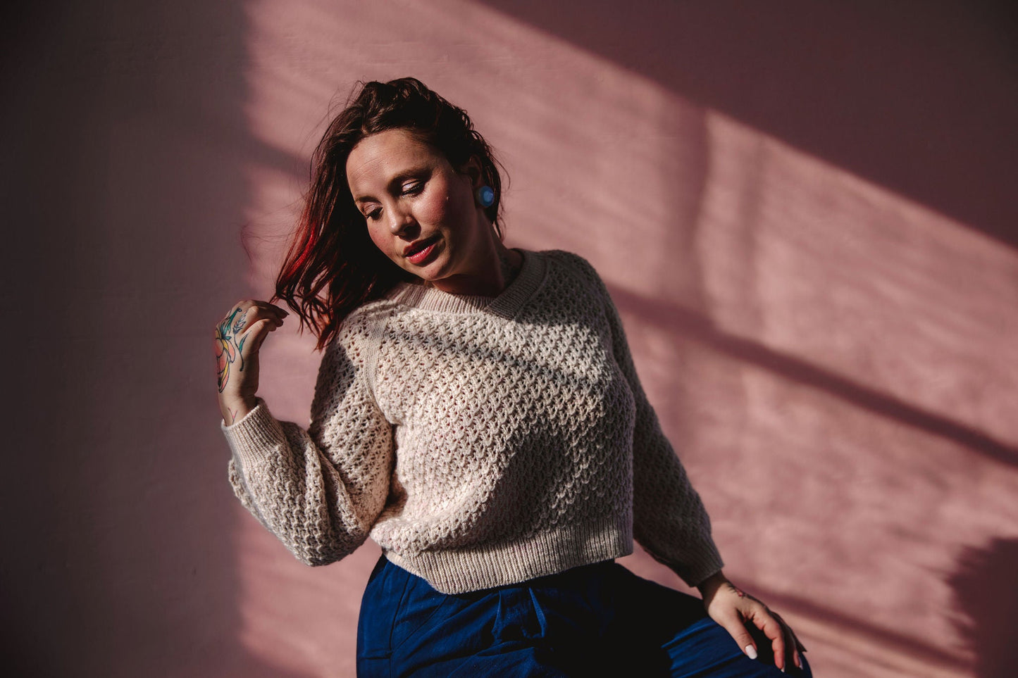 Bess stands outside, with the sun casting shadows over her. She wears a cream colored lace knit raglan sweater.