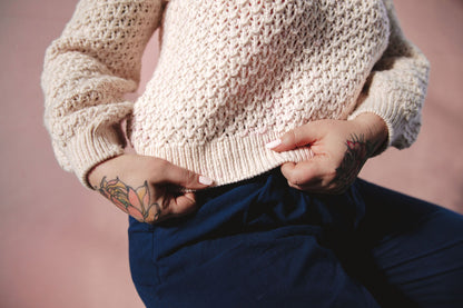 Seen from the shoulders down at a 3/4 angle, Bess wears a cream colored raglan with an allover knit lace design.