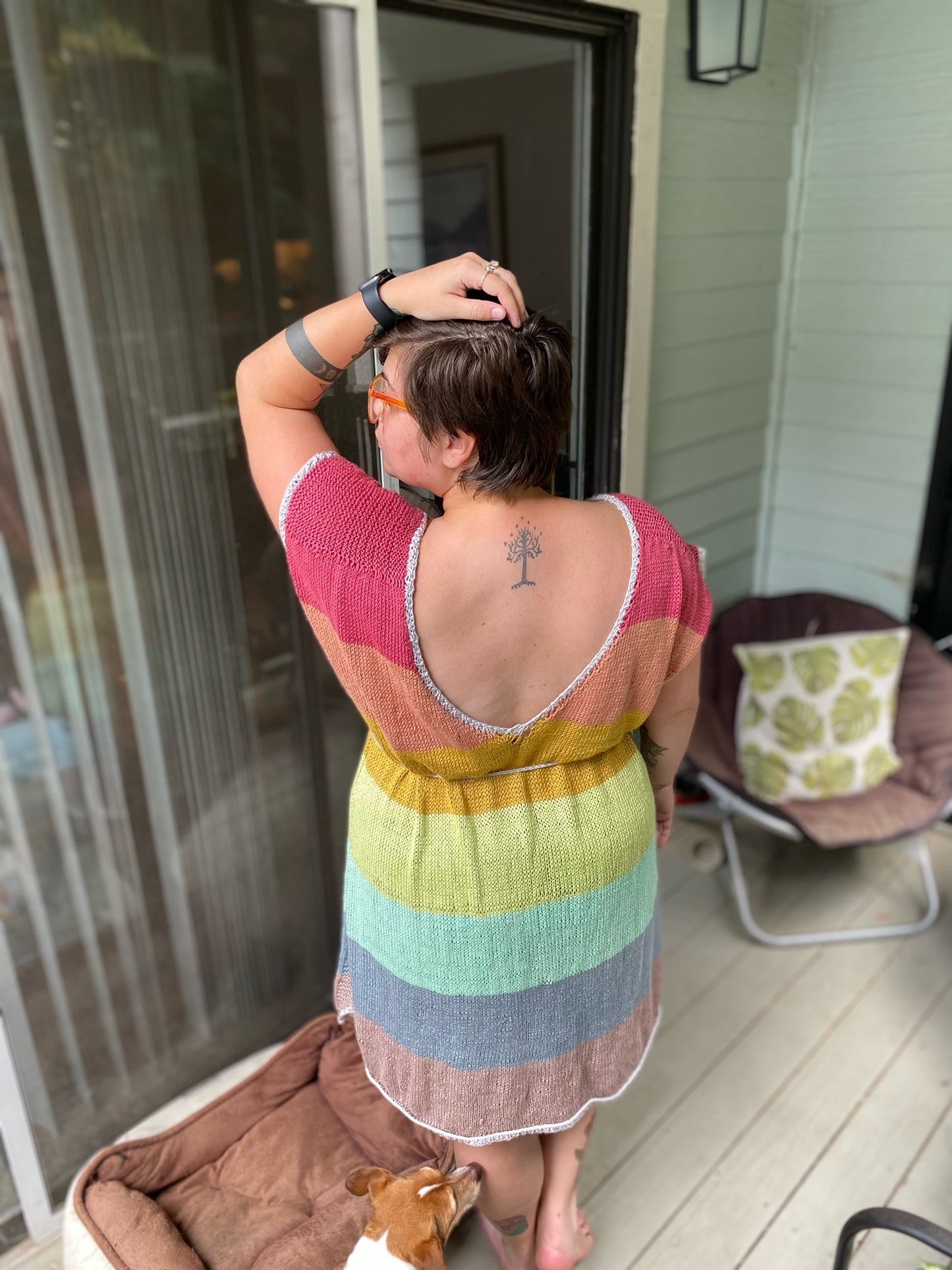 Seen from behind, a person wears a handmade dress, knit using rainbow yarn.